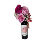 The Wine and Flowers gift features a Cabernet wine bottle decorated with pink and purple roses, Valentine’s Day flowers, baby’s breath, heart-shaped tags, and a charming "Love Potion" label.