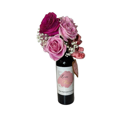 The Wine and Flowers gift features a Cabernet wine bottle decorated with pink and purple roses, Valentine’s Day flowers, baby’s breath, heart-shaped tags, and a charming "Love Potion" label.