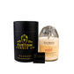 A Recycled Cognac Candle in a Rémy Martin 1738 bottle sits beside a black Custom Candle Co. container, with a business card displayed in front.