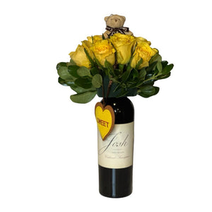 The "Wine and Flowers" arrangement features a Cabernet wine bottle adorned with yellow roses, greenery, a small teddy bear, and a heart-shaped "SWEET" tag—making it a charming romantic gift or Valentine’s Day floral surprise.