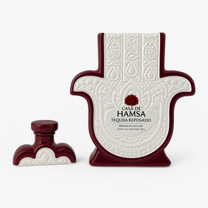 The Recycled Reposado Tequila Candle comes in a ceramic Hamsa hand bottle with ornate patterns and a matching cap—add a unique touch to your space by using it as a candle or decorative piece once empty.