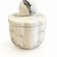 The Marble Luxe Candle is a round, white ceramic container with a black marbled pattern, matching lid, and spherical handle, shown against a plain white background.