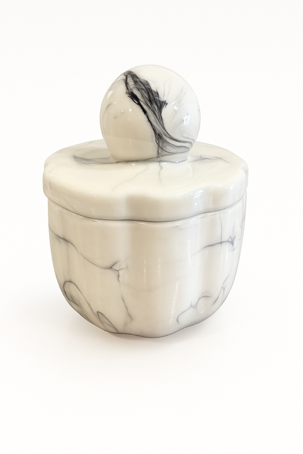 The Marble Luxe Candle is a round, white ceramic container with a black marbled pattern, matching lid, and spherical handle, shown against a plain white background.