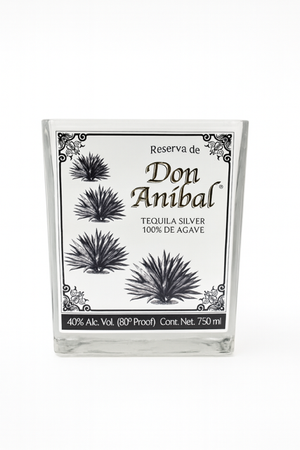 The Recycled Silver Tequila Candle features a clear glass bottle with black agave plant illustrations and a decorative border on the label, inspired by Don Anibal Silver Tequila (100% agave, 40% ABV, 750 ml).