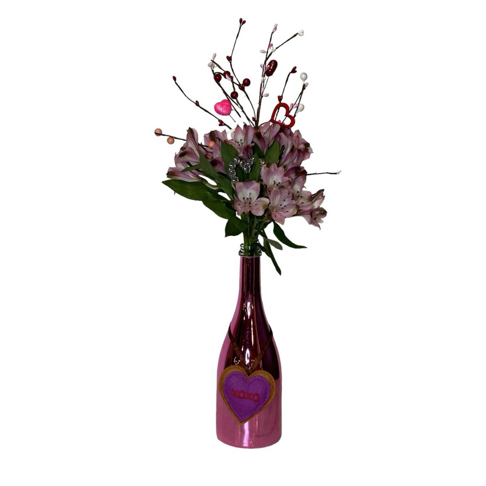 Valentine Bouquets: Pink flowers and decorative branches in a repurposed bottle vase labeled "XOXO"—a charming, eco-friendly arrangement perfect for Valentine’s Day.