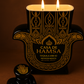 A Recycled Black and Gold Tequila Candle made from Coconut Apricot wax, labeled "Casa de Hamsa," sits next to a matching black decorative stopper, both set against a brown background.
