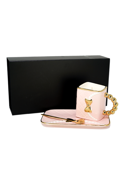 The 3D Design Handbag Shaped Ceramic Coffee Cups Set features a pink and gold cup with a decorative handle, matching rectangular tray, gold spoon, and comes in a black box—an elegant and practical decorative gift.