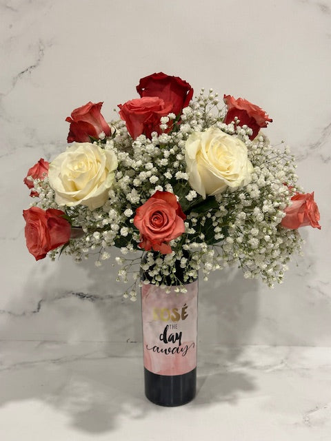 Wine and Flowers: A romantic bouquet of red, white, and pink roses with baby's breath in a glass vase labeled "Rosé the day away"—the perfect Valentine’s Day gift or centerpiece against a light marble backdrop.