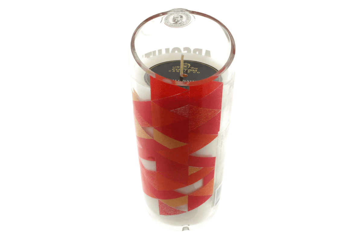 The Recycled Ruby Vodka Candle by Custom Candle Co. is a hand-poured white soy candle in a glass vessel featuring a red and orange geometric label, with a single wick visible at the top.