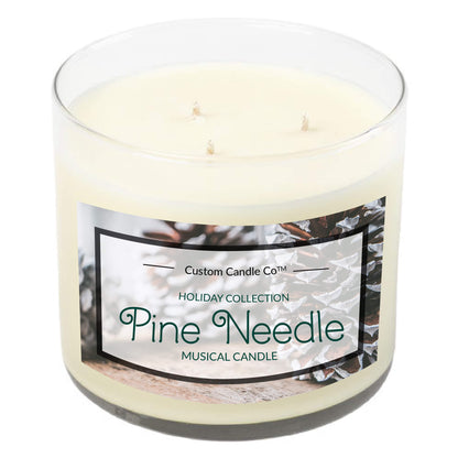 The Musical Holiday Candle – Pine Needle from the Custom Candle Co. Holiday Collection features a white three-wick design in a clear glass jar with pinecone and branch imagery—a festive scented accent for your home.