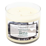 The Musical Holiday Candle – Slate by Custom Candle Co. features a three-wick white soy candle in a glass jar with a winter scene—perfect for fans of scented holiday candles from the Holiday Collection.