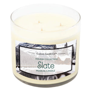 The Musical Holiday Candle – Slate by Custom Candle Co. features a three-wick white soy candle in a glass jar with a winter scene—perfect for fans of scented holiday candles from the Holiday Collection.