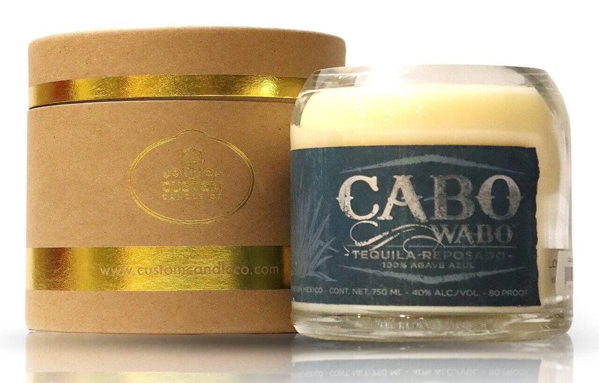 The Recycled Azul Agave Reposado Tequila Candle, in a glass labeled "Cabo Wabo Tequila Reposado," sits beside a gold-accented cylindrical box, making it the perfect eco-friendly decor accent.