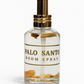 Clear glass bottle labeled "Palo Santo Box Set" with gold details and visible wood pieces inside, set against a white background.