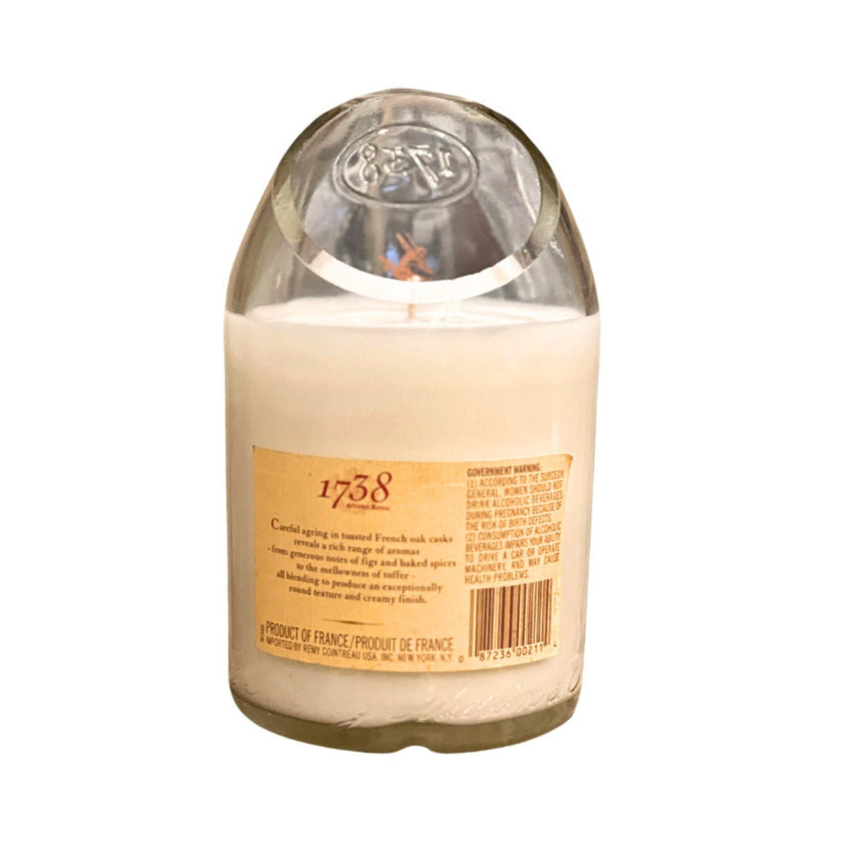 The Recycled Cognac Candle features coconut-apricot wax in a clear glass container with a white finish, an embossed lid, and a tan label marked 1738, designed to evoke the look of cognac bottle candles.