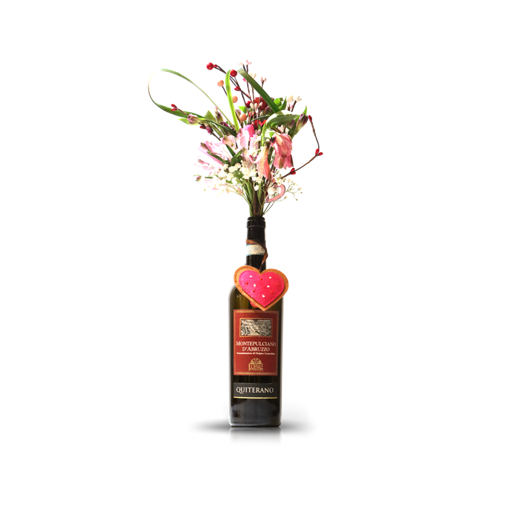 The Valentine Bouquets feature pink and white flowers in a repurposed bottle vase, accented with a heart-shaped cookie—an eco-friendly and sustainable Valentine’s Day gift.