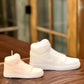 A large AJ-1 White Hightop Sneaker Candle, hand poured and shaped like a sneaker, sits on a wooden surface with a blurred background.