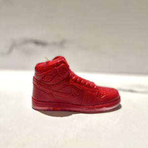 The AJ-1 Red Hightop Sneaker Candle – Large (On Backorder), hand poured and infused with Black Ice scent, is shown on a white surface against a blurred gray background.
