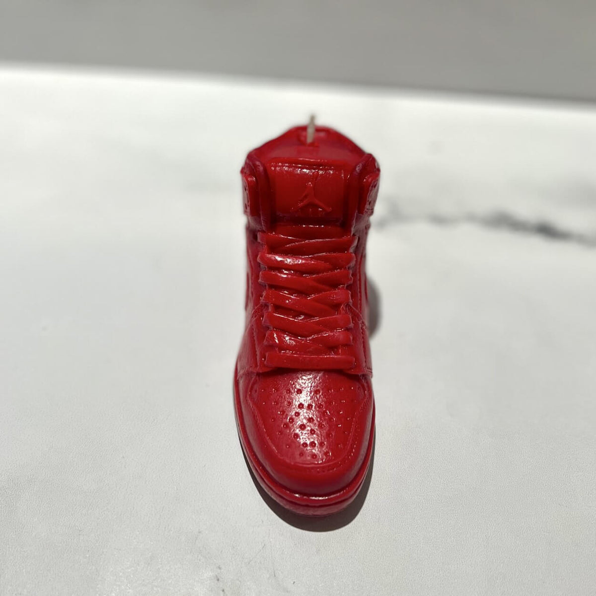 The AJ-1 Red Hightop Sneaker Candle – Large (On Backorder) is a hand-poured candle shaped like a red high-top sneaker, infused with Black Ice fragrance and displayed on a white surface.