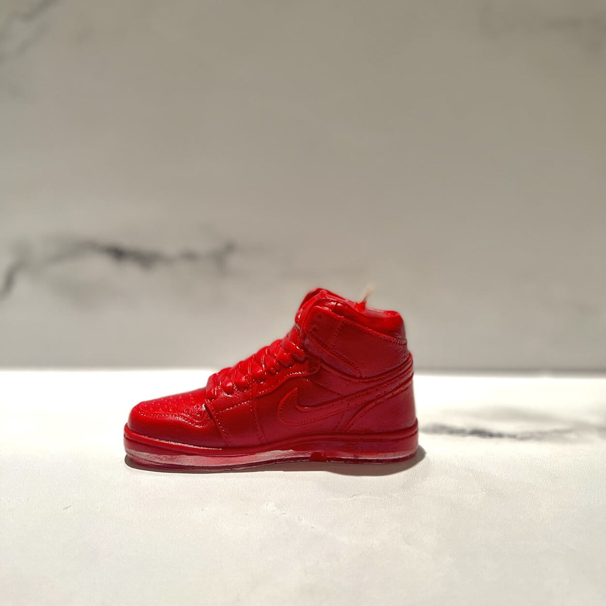 The AJ-1 Red Hightop Sneaker Candle – Large (On Backorder), hand poured and scented with fresh Black Ice, sits on a light surface against a neutral, subtly marbled background.