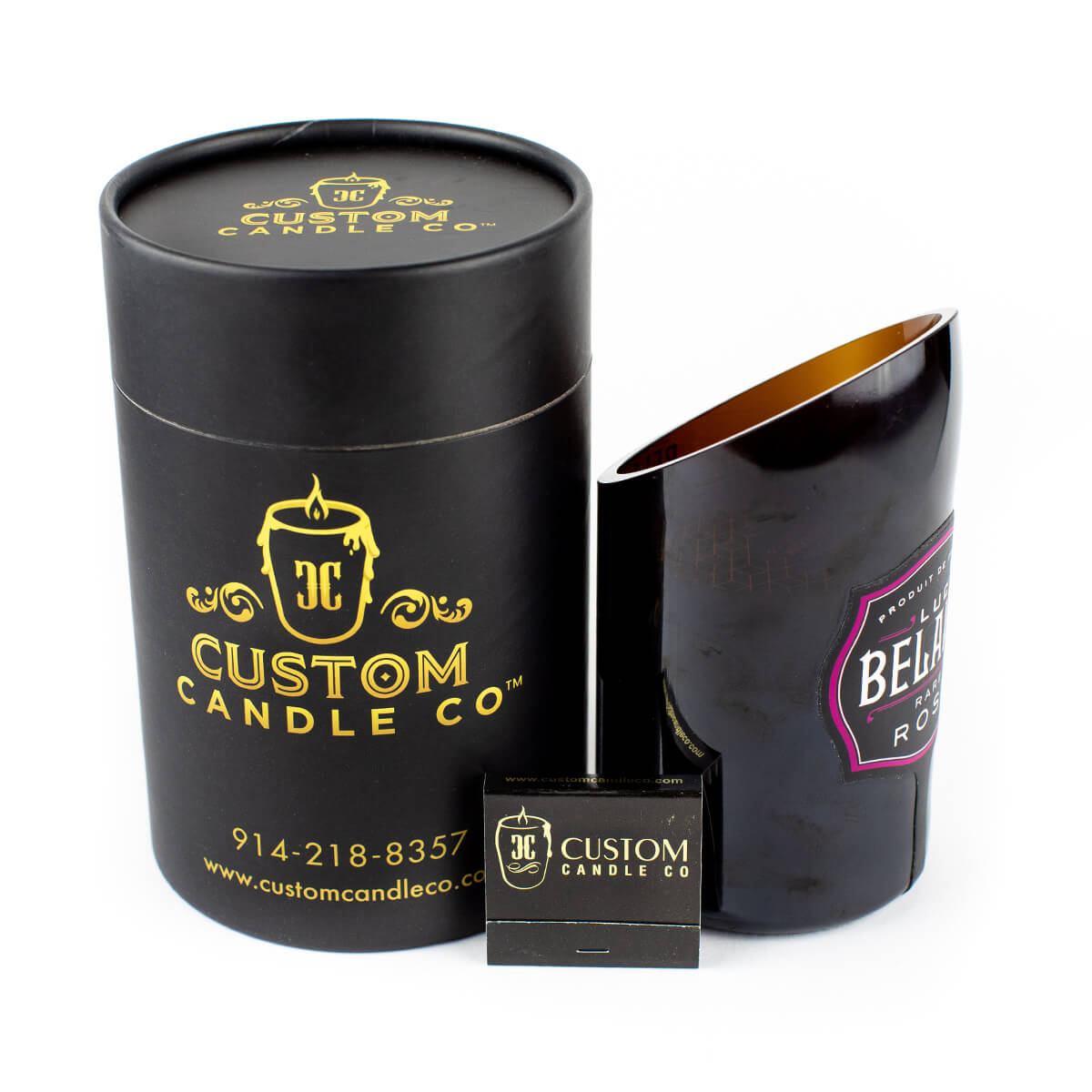 A black cylindrical box labeled "Custom Candle Co" with a Recycled Rare Rosé Champagne Candle in a cut bottle sits next to a branded matchbox.