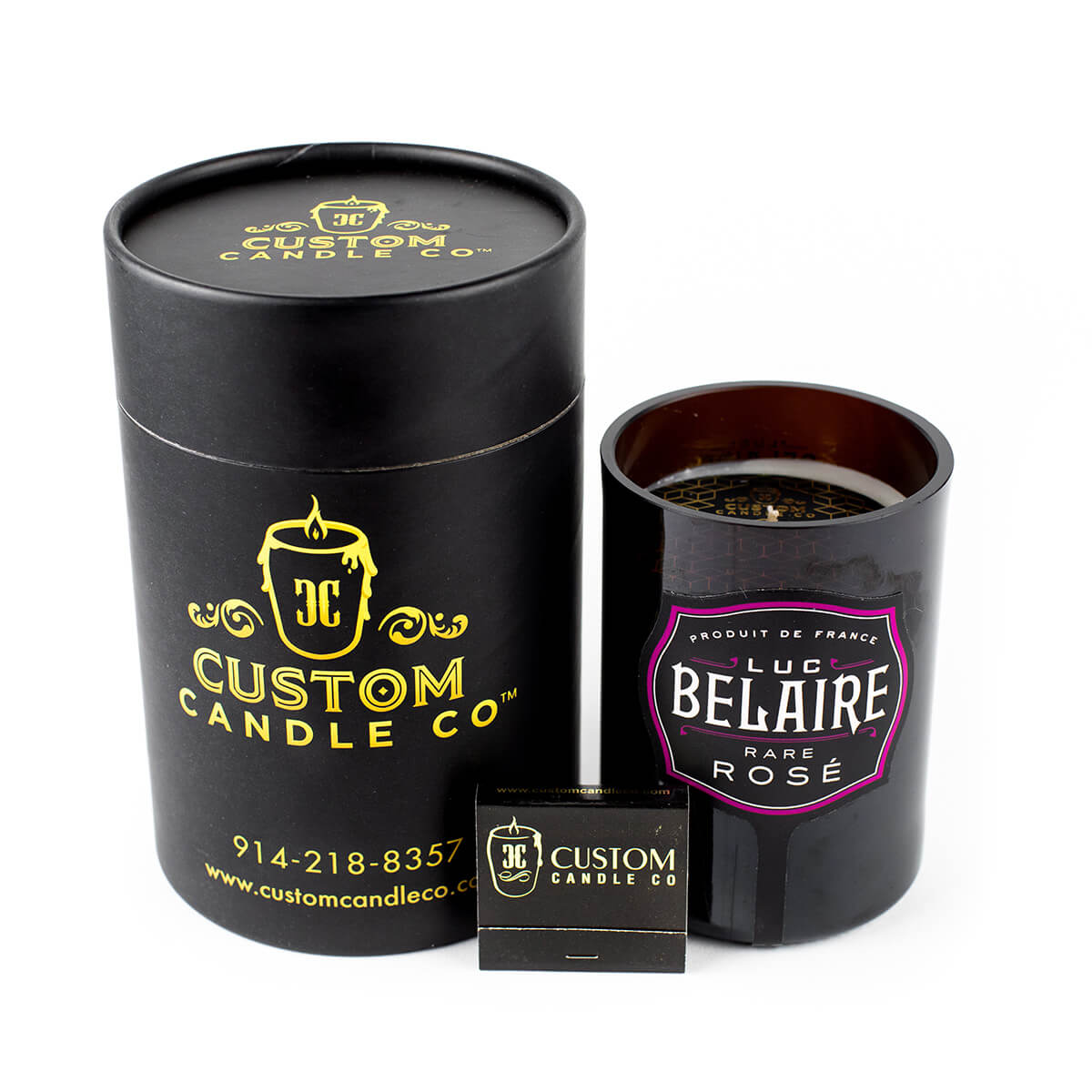 A black cylindrical "Custom Candle Co." container sits beside a Recycled Rare Rosé Champagne Candle and a small black matchbox.