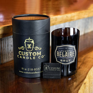 The Recycled Black Champagne Candle, an all-natural soy candle by Custom Candle Co., is set in a cut Luc Belaire Brut bottle and paired with a branded matchbox on a wooden surface.