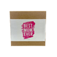A brown box with a white label that says "Best Mom Ever" in bold pink letters—featuring the Best Mom Ever candle, lavender violet scented and made from soy wax. Perfect Mother’s Day gift. Product: Best Mom Ever, Pink Design with Brown Box.