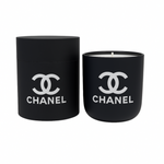 The Black Ceramic Designer Candle sits beside its matching cylindrical container, both in black ceramic and decorated with the white Chanel logo.
