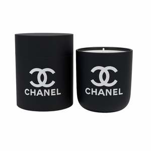 The Black Ceramic Designer Candle sits beside its matching cylindrical container, both in black ceramic and decorated with the white Chanel logo.
