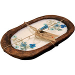 The Blue Floral Wood Candle – Floral Scented is an oval soy wax candle topped with dried blue flowers and leaves, set in a wooden tray, tied with twine, and finished with a gift tag—ideal for rustic centerpieces.
