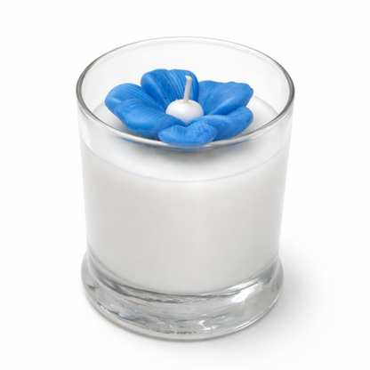 The Blue Blossom Candle is a handcrafted white soy candle in a clear glass holder, topped with a blue flower-shaped decoration and wick.