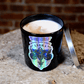 The Zodiac: Libra Candle, a black soy jar with a silver lid, sits on wood against a brick wall—adding charm to this zodiac-inspired candle.