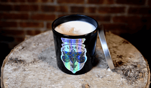 The Zodiac: Libra Candle, a black soy jar with a silver lid, sits on wood against a brick wall—adding charm to this zodiac-inspired candle.