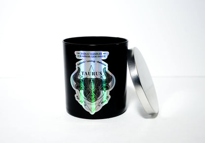 The Zodiac: Taurus Candle is a black jar soy candle with a metallic lid, holographic Taurus label, and text hinting at a surprise gem inside—crafted for an enchanting touch.