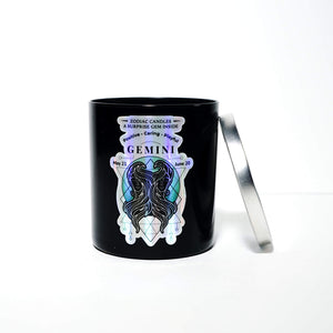 The Zodiac: Gemini Candle is a black jar labeled "Gemini," featuring an illustrated Gemini figure and symbol. It sits on a white background with its partially open silver lid resting beside it.