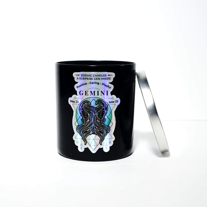 The Zodiac: Gemini Candle is a black jar labeled "Gemini," featuring an illustrated Gemini figure and symbol. It sits on a white background with its partially open silver lid resting beside it.