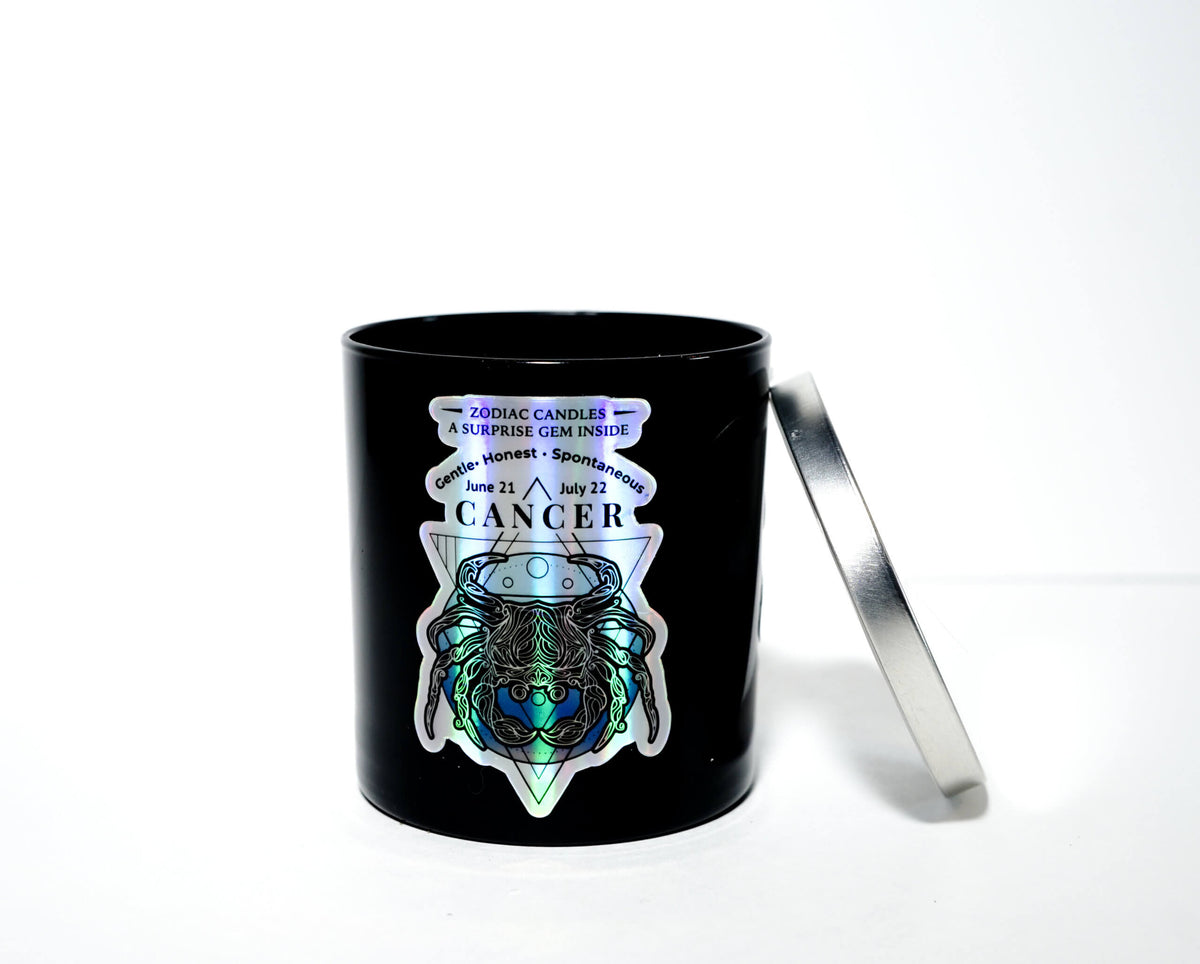 The Zodiac: Cancer Candle is a black soy jar with a silver lid, featuring a holographic crab, crystal, zodiac dates, and "Zodiac Candles" on the front—an ideal gift for anyone with the Cancer zodiac sign.