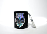 The Zodiac: Aries Candle features a black jar with a ram graphic and zodiac dates beside a silver lid on a white background—a chic soy candle ideal for astrology lovers.