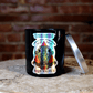 The Zodiac: Aquarius Candle, made from natural soy, sits on a wooden surface with its vibrant zodiac label visible and the silver lid placed nearby.