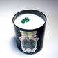 The Zodiac: Gemini Candle is a black, natural soy candle with a zodiac label and two green gemstones set in white wax.