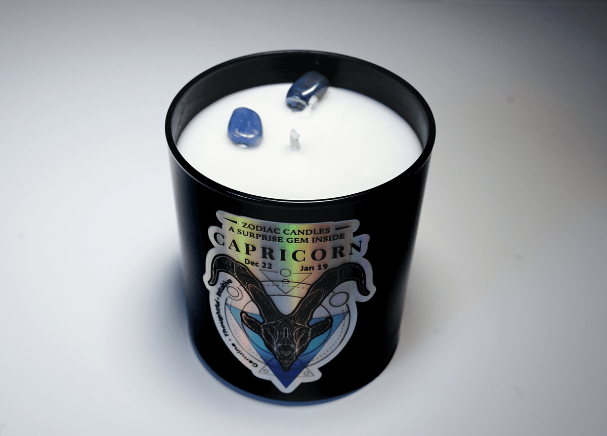The Zodiac: Capricorn Candle features black wax, white soy interior, two blue crystals on top, and a label with zodiac dates (Dec 22–Jan 19)—an ideal candle for any Capricorn.