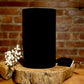 The “Thanks for Puttin’ Up with My Shit” large black soy candle, made from a recycled wine bottle, rests on a wooden slab with dried white flowers and a metal wick trimmer against a brick wall backdrop.