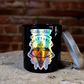 The Zodiac: Sagittarius Candle features a black jar with zodiac-themed artwork and a silver lid, creating a striking celestial accent on any wooden surface against a brick wall.