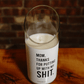 A Thanks for Puttin’ Up with My Shit soy candle in a recycled wine bottle holder rests on wood, its cheeky label displayed. A brick wall appears in the background.