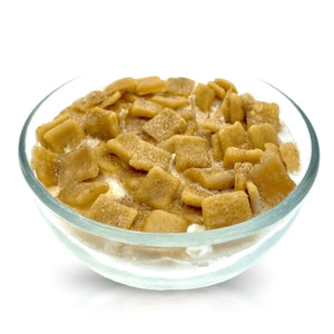 A clear glass reusable bowl contains the Cereal Cinnamon Crunchy Candle, which looks like milk topped with square-shaped cinnamon cereal pieces.