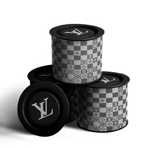 Four Checkered Designer Tin Candles with black lids, showcasing a gray checkerboard pattern with LV monogram and floral motifs, are stacked against a white background. Each is made with natural soy wax and a pure cotton wick.