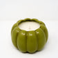 The Ceramic Pumpkin Vessel Candle, featuring natural soy wax in a white ceramic pumpkin, sits on a white surface and evokes autumn’s charm with its seasonal scent against a simple backdrop.