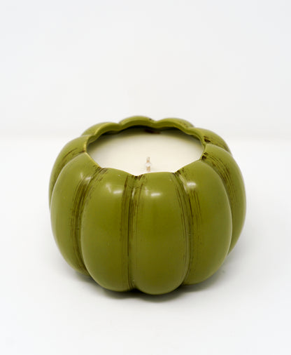 The Ceramic Pumpkin Vessel Candle features a green, pumpkin-shaped ceramic container with a white candle inside, ideal for autumn scents. Shown here against a plain white background.