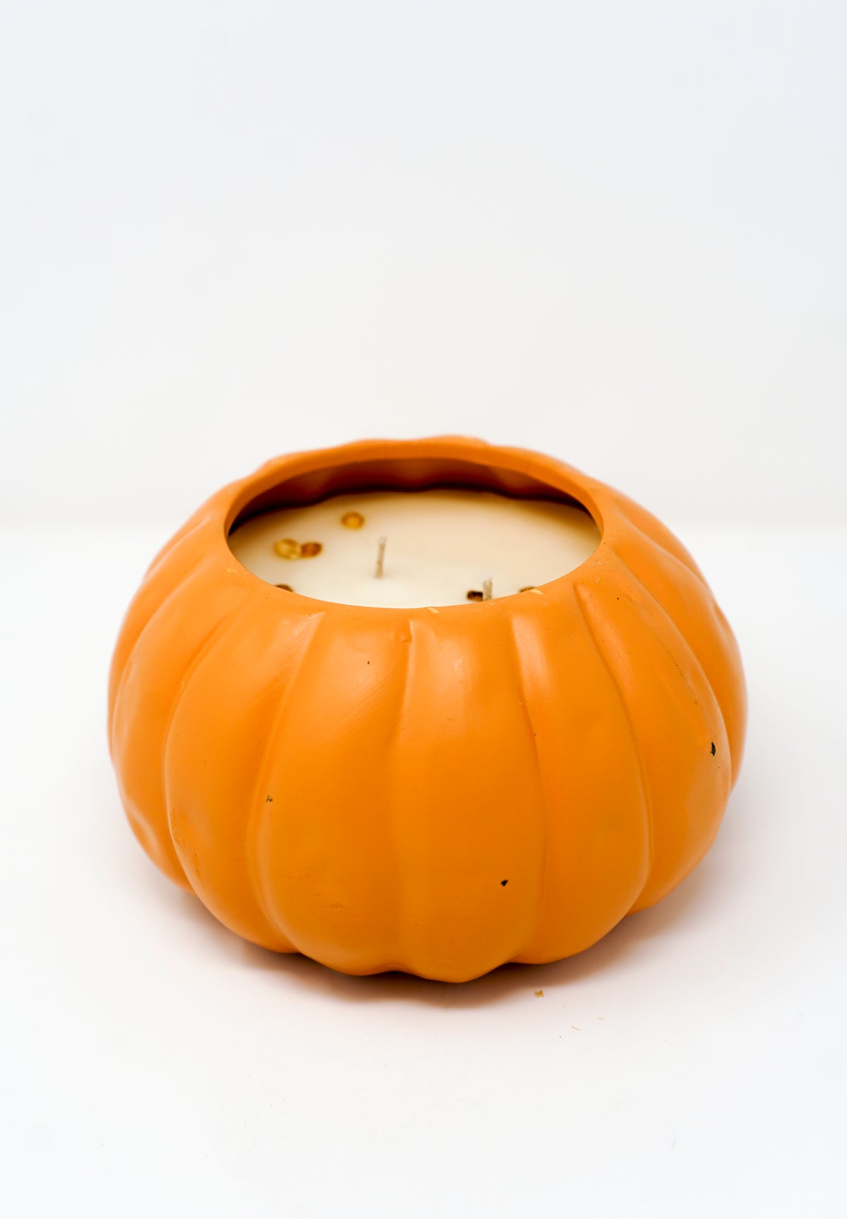 A partially used white soy wax candle is housed in a pumpkin-shaped orange ceramic Pumpkin Vessel Candle, shown against a plain white background.